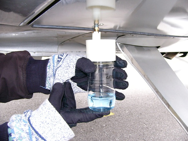  Pegando uma amostra de combustível do dreno de intradorso do American Aviation AA-1 Yankee usando um recipiente GATS para coleta de combustível. 